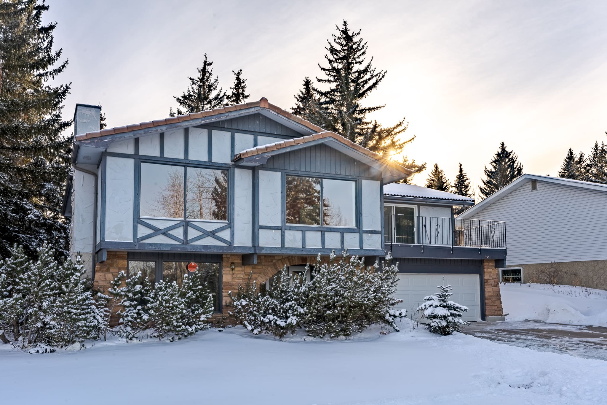 A house with snow on the ground and trees in front of it.