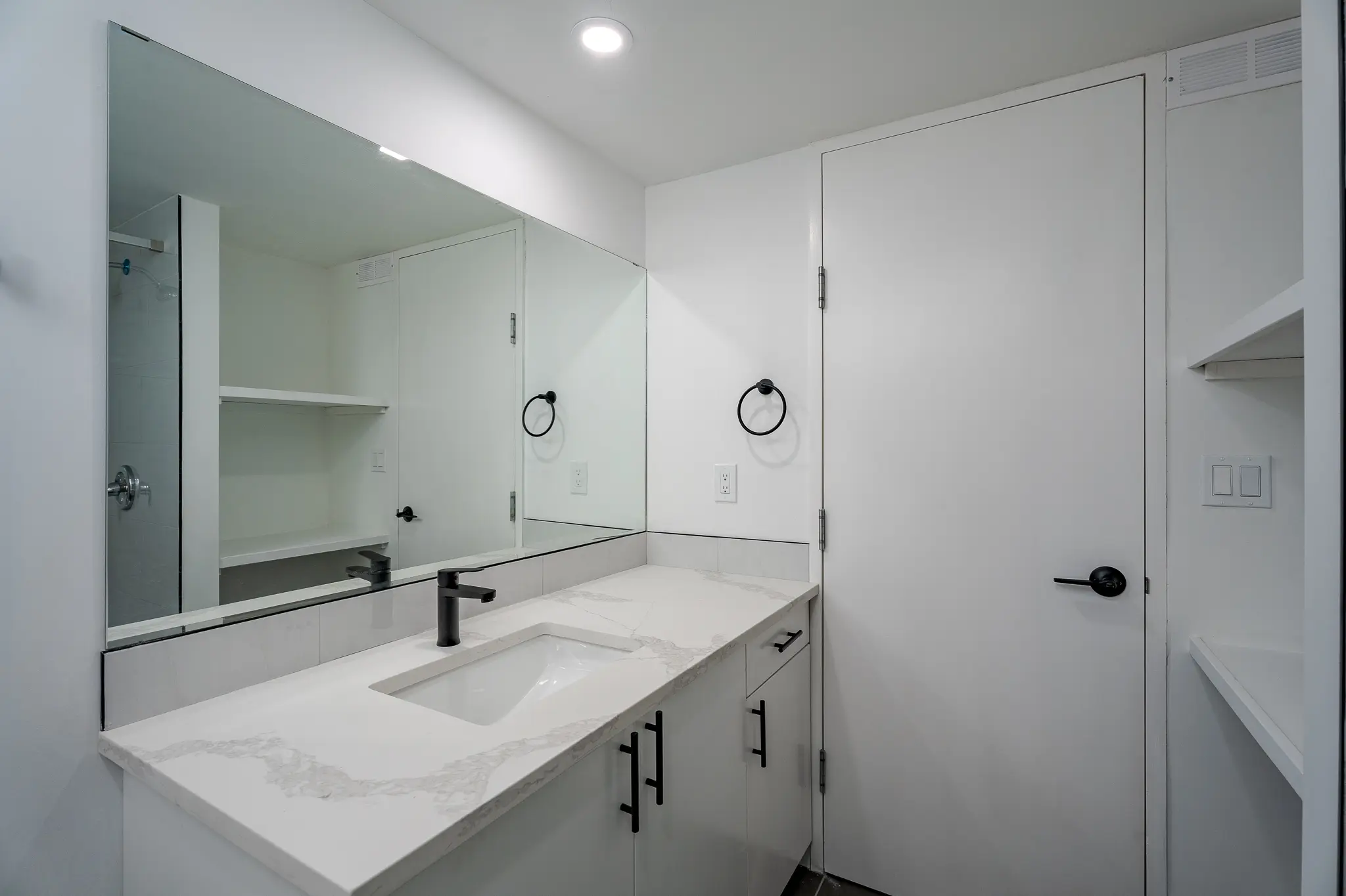 A bathroom with white walls and a large mirror.