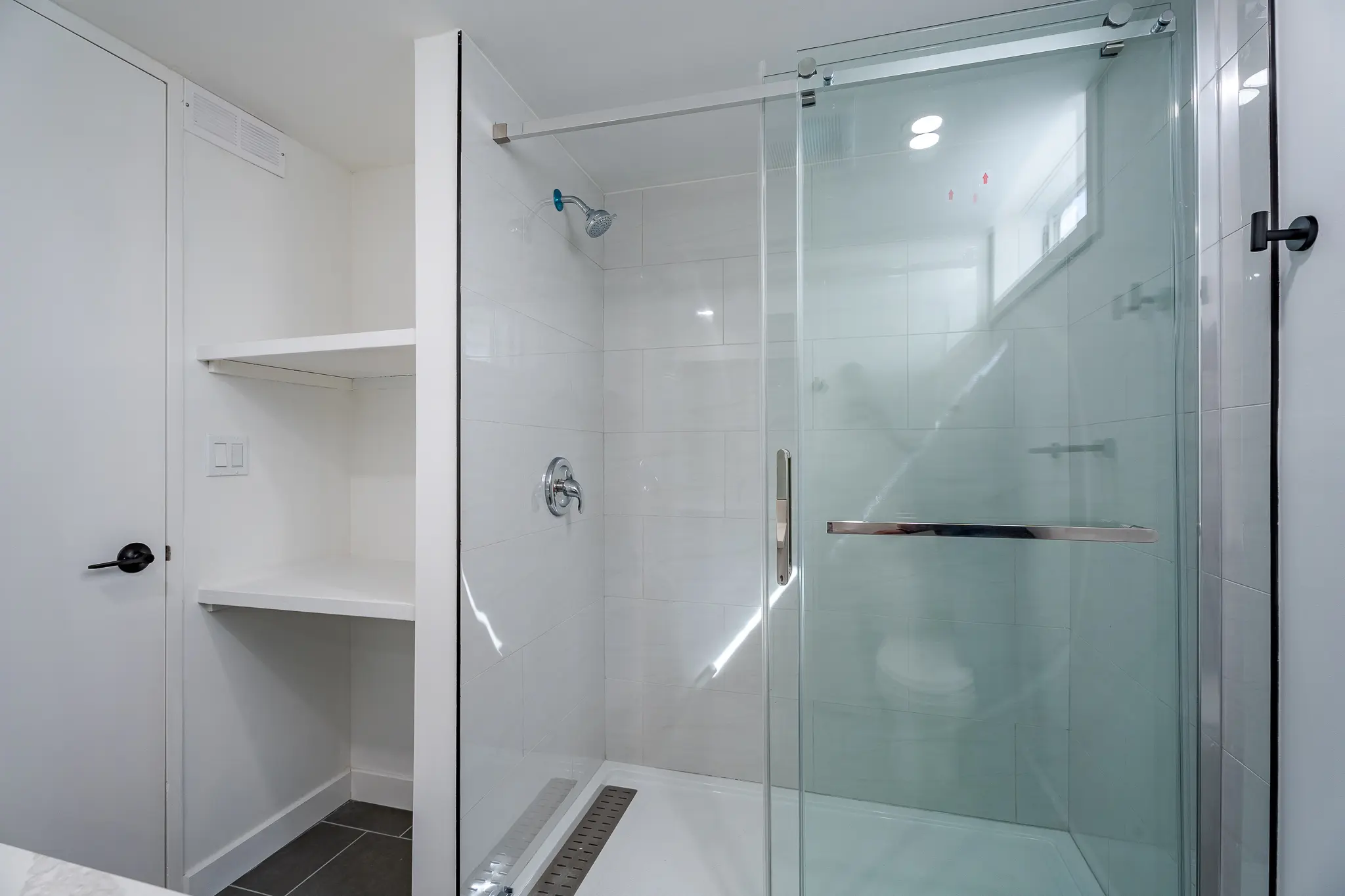 A white shower with glass doors and shelves.