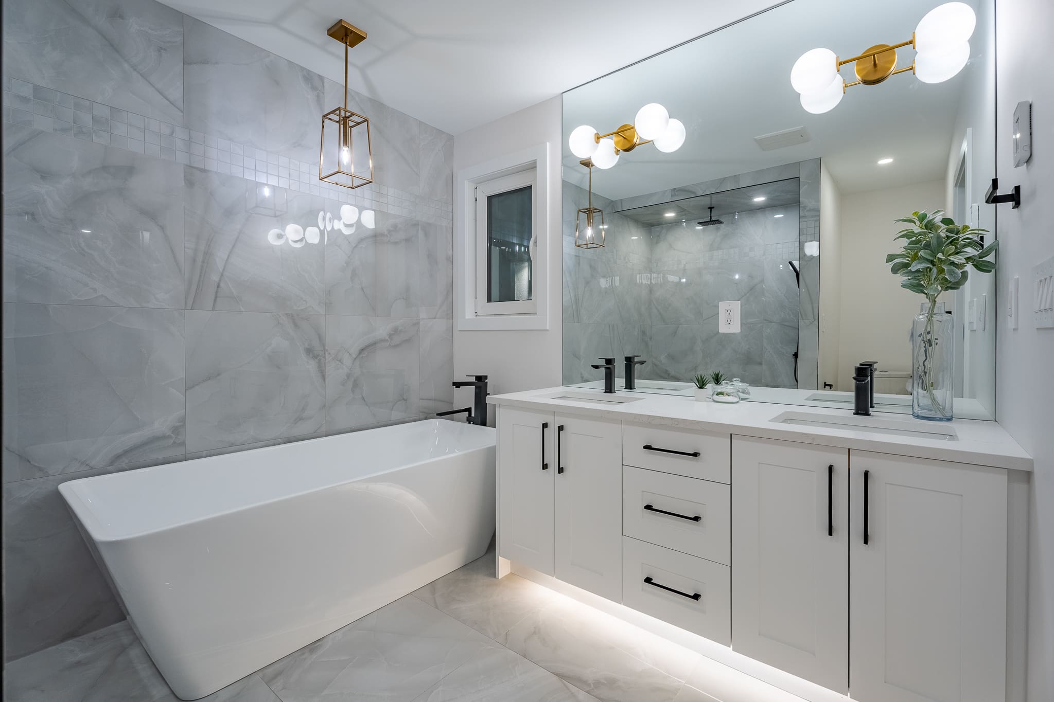 A bathroom with marble walls and floors, white cabinets and lights.