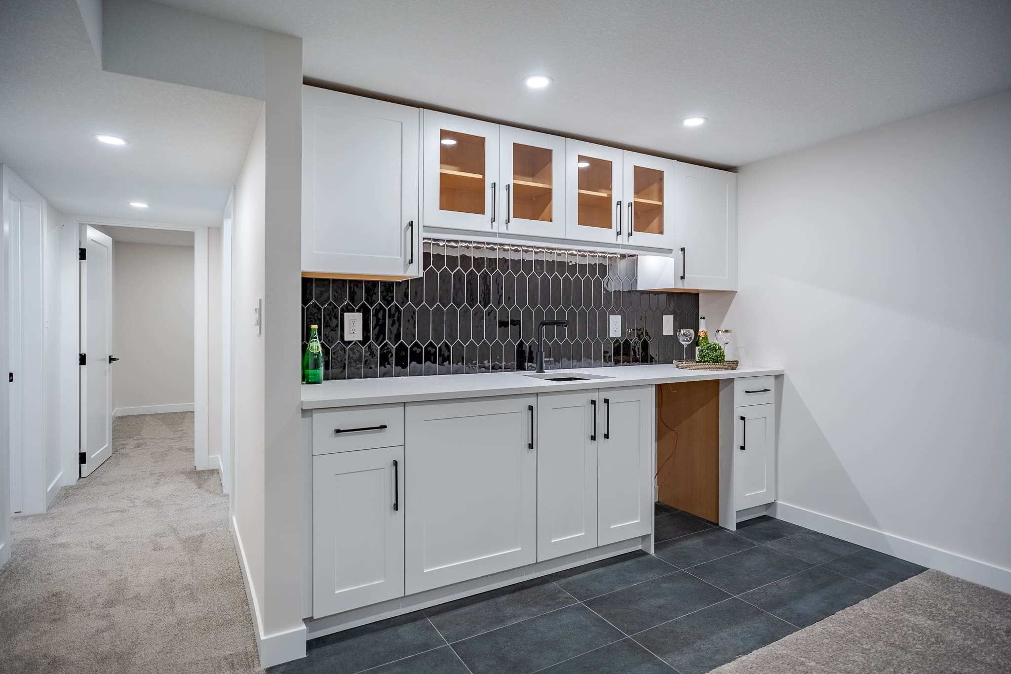 A kitchen with white cabinets and black tile backsplash.